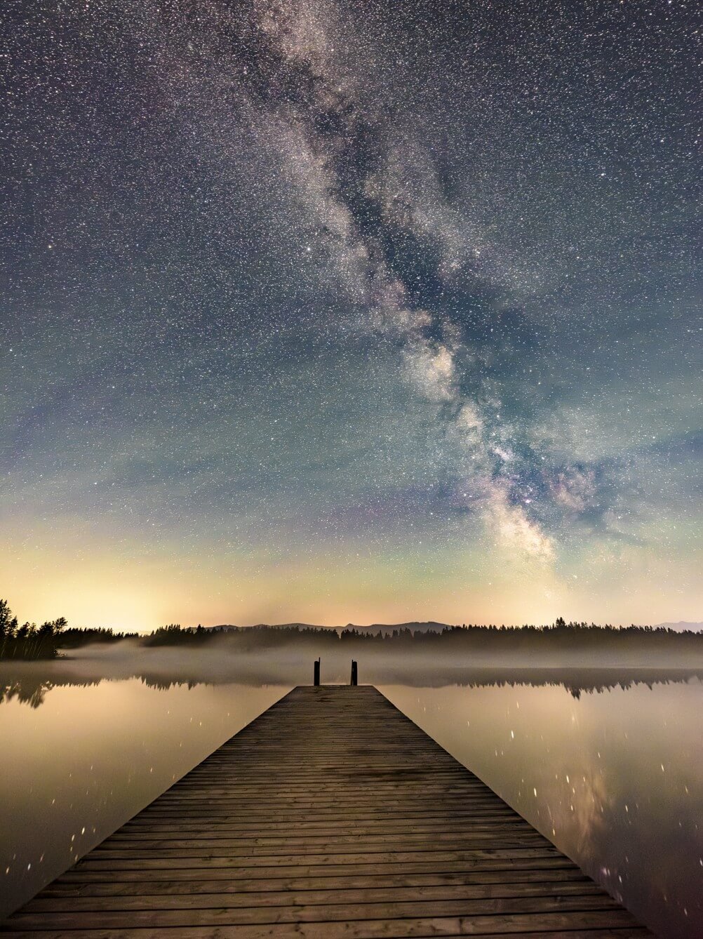 Ein Holzsteg führt in den Kirchsee, über dem die Milchstraße am nächtlichen Sternenhimmel leuchtet.